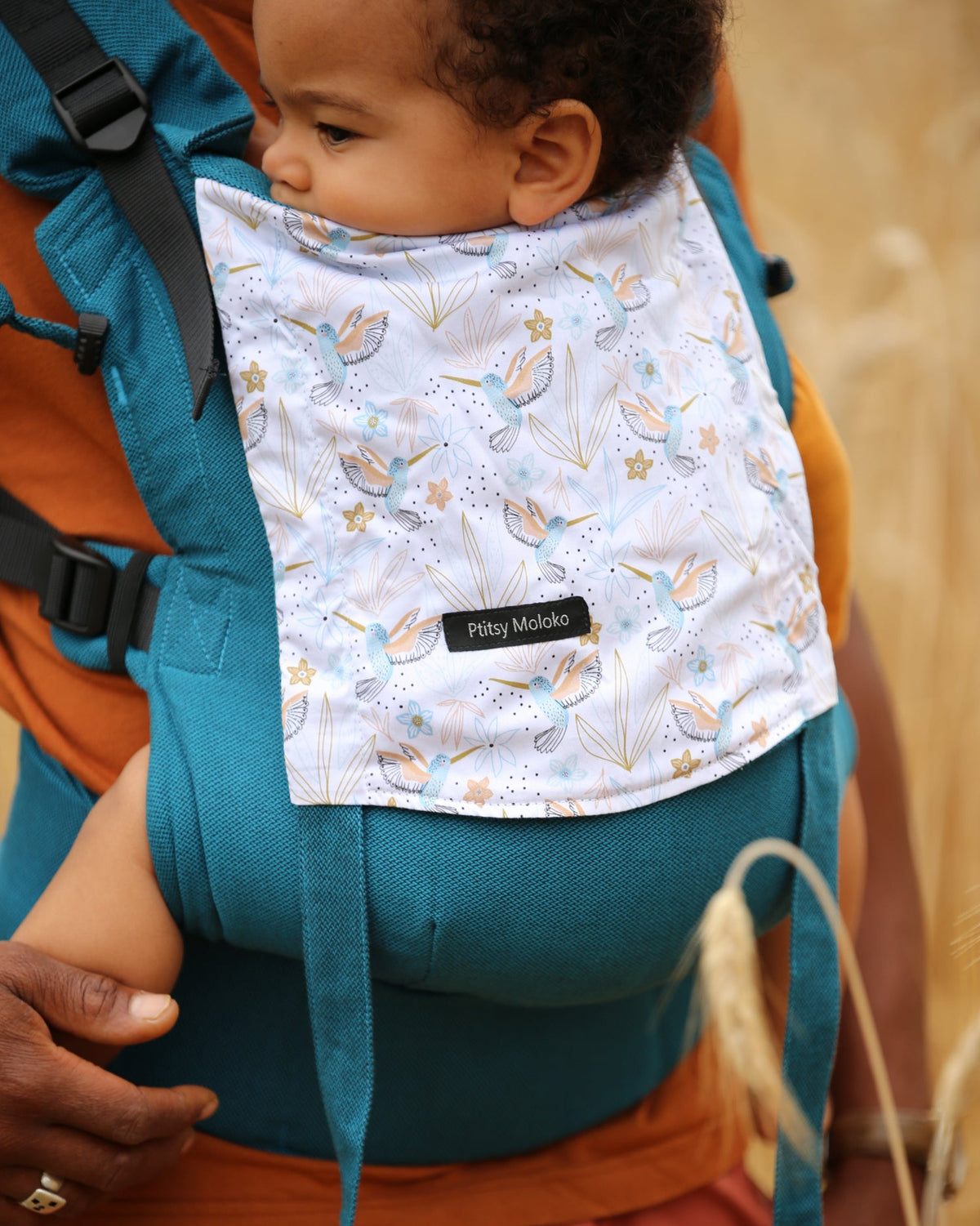 Porte-bebe en coton bio avec jolis motifs colibris sur fond bleu mediterranée. Très confortable et facile à installer.