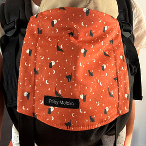 Porte-bebe naissance avec têtière motifs chats noirs et lunes beiges sur fond orange. Tissu de base en coton biologique noir.